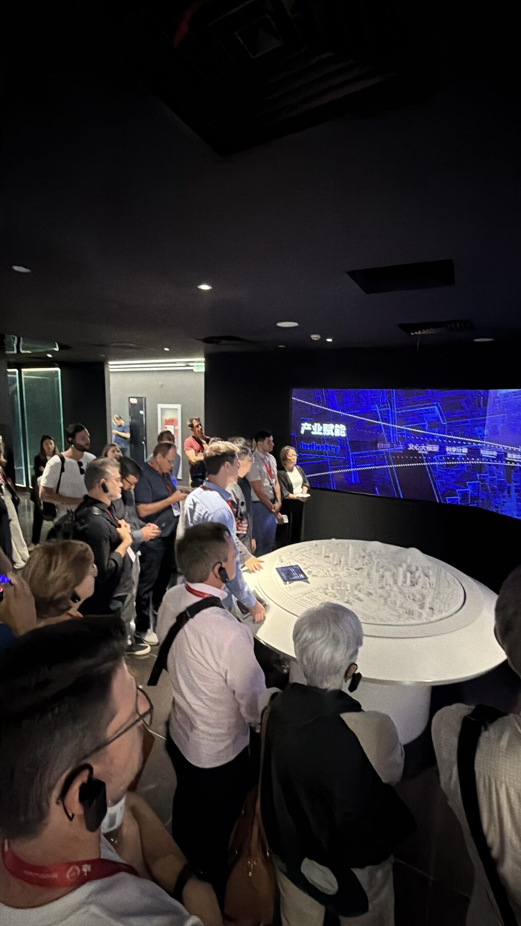 Delegação brasileira em tour guiado dentro de uma big tech chinesa, observando uma maquete tecnológica