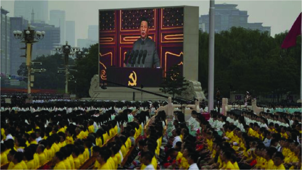 Um grande grupo de pessoas com camisas amarelas em frente a uma grande tela comemorando o 100º aniversário do Partido Comunista da China: História, Conquistas e Perspectivas.