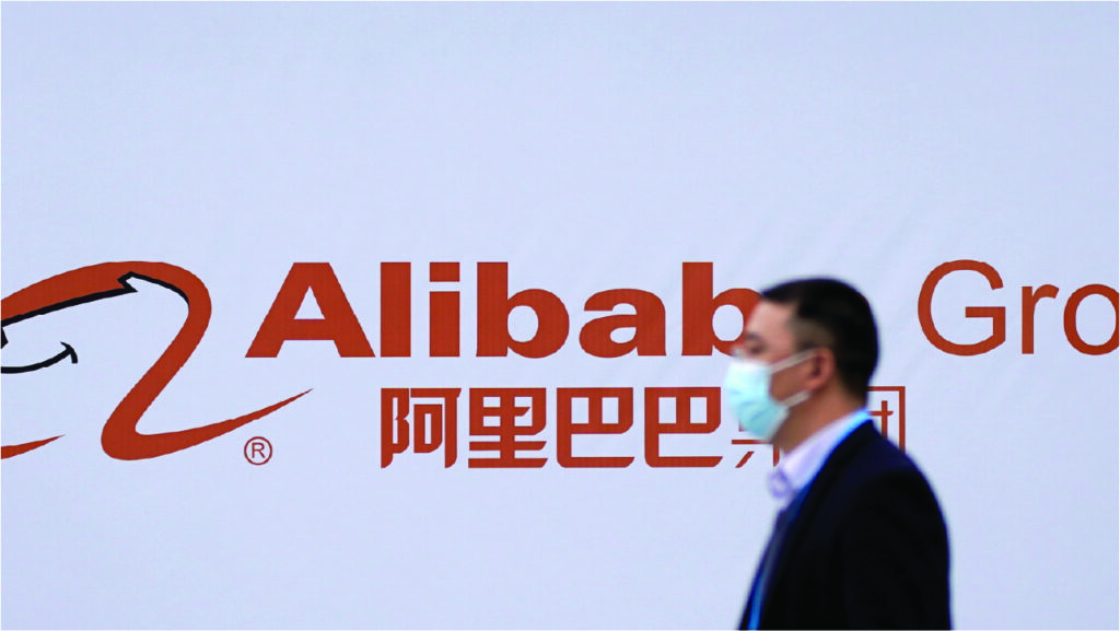 Um homem usando máscara passa pelo logotipo do Grupo Alibaba, pensando em como calcular o custo de envio de um produto do Alibaba para o Brasil.