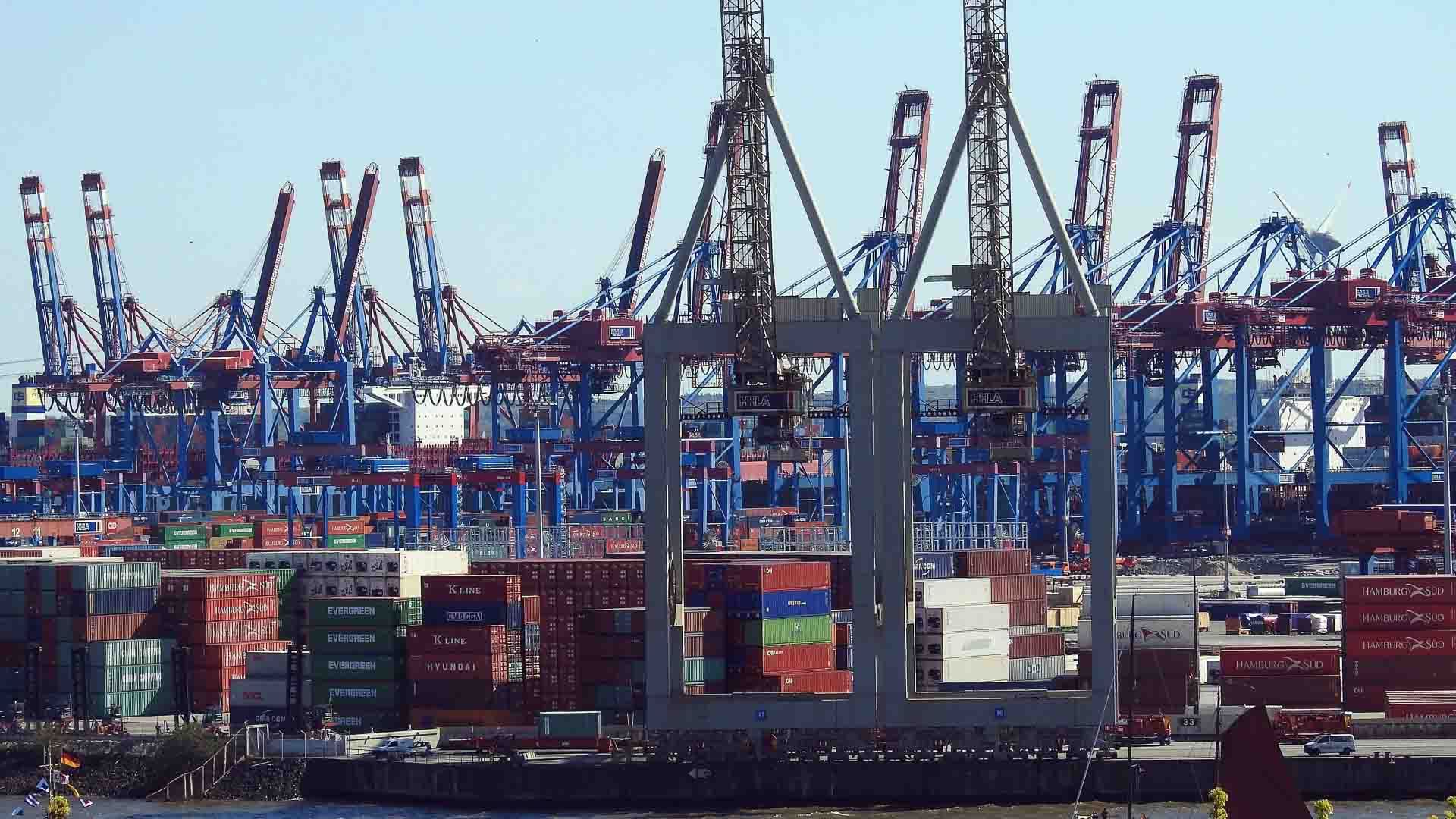 Um movimentado porto de embarque prospera em meio ao caos, com vários guindastes e contêineres de carga empilhados, demonstrando uma prova de resiliência enquanto "Cresça na Crise" orienta as operações e as relações continuam inabaláveis.