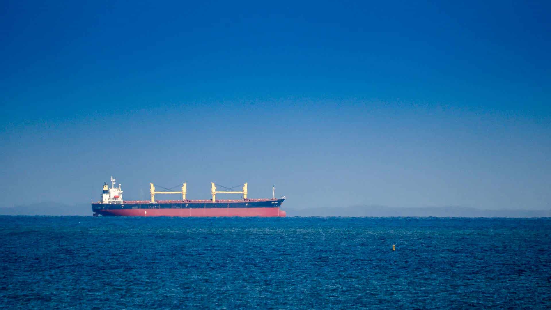 Um grande navio de carga, carregado de produtos solares, navega em um mar azul calmo sob um céu limpo.