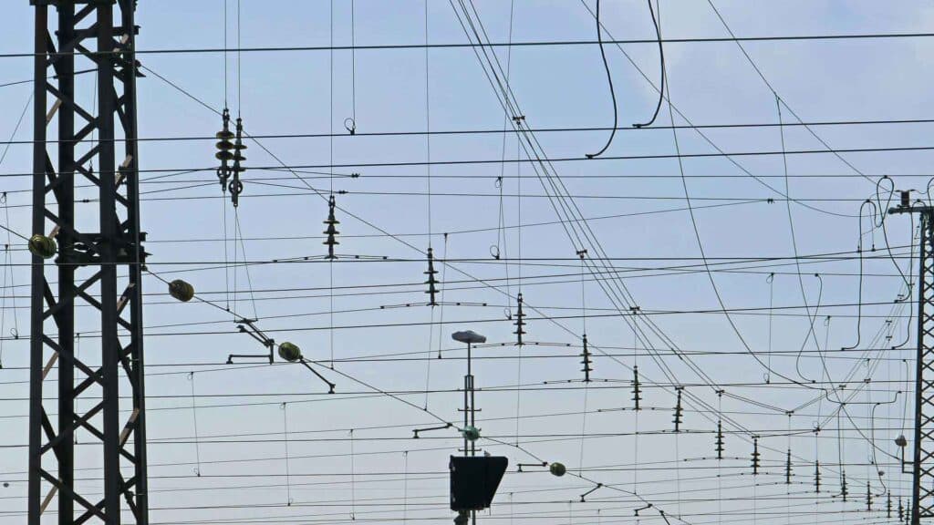 Close de uma rede de linhas de energia aéreas com estruturas de suporte contra um céu limpo, lembrando as conexões complexas encontradas nas vibrantes cidades da China.