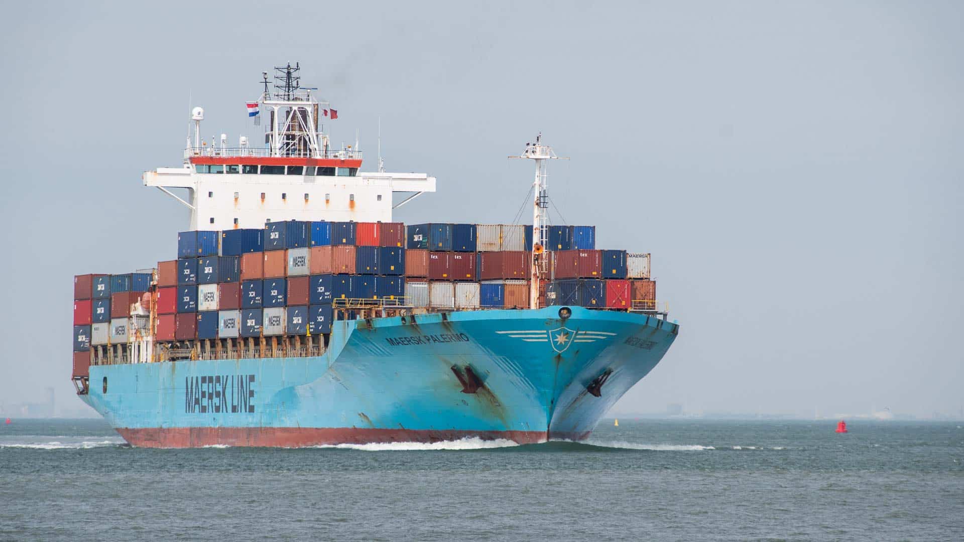 Um grande navio de carga carregado com contêineres coloridos empilhados navega por um corpo de água sob um céu limpo, lembrando uma viagem à China.