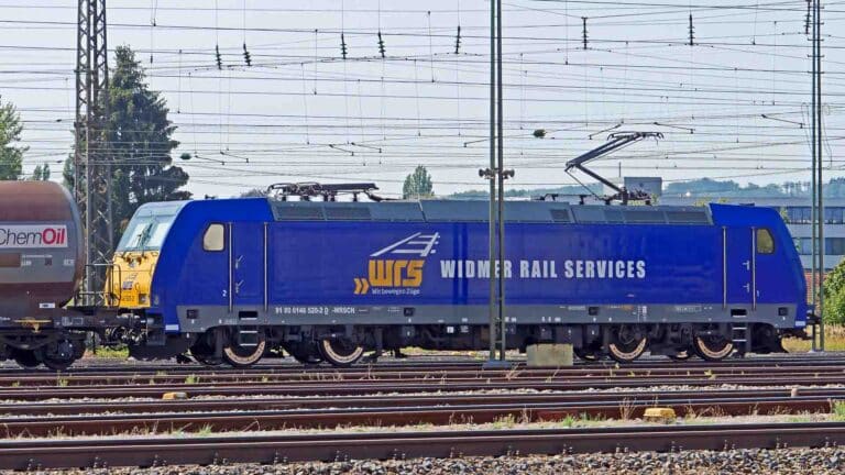 A locomotiva Blue Widmer Rail Services, deslizando sob fios aéreos perto de um vagão-tanque da ChemOil em um dia ensolarado, destaca os avanços essenciais no transporte ferroviário esperados até 2025.