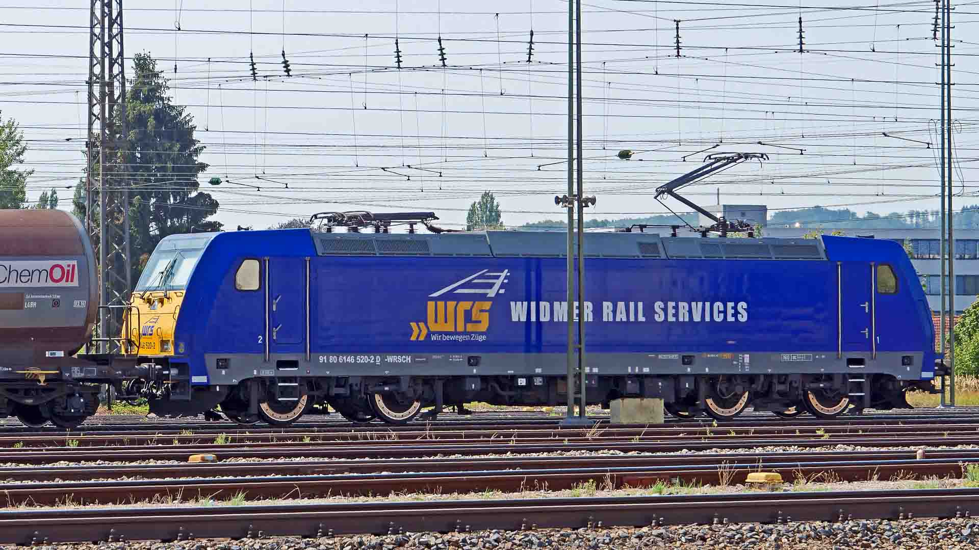 A locomotiva Blue Widmer Rail Services, deslizando sob fios aéreos perto de um vagão-tanque da ChemOil em um dia ensolarado, destaca os avanços essenciais no transporte ferroviário esperados até 2025.