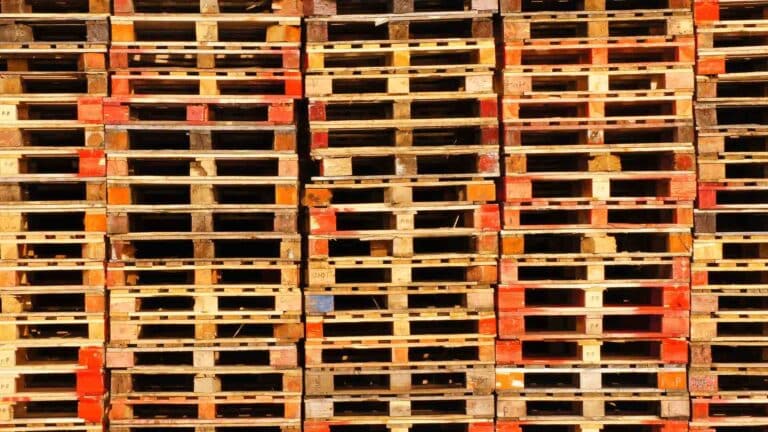 Pilhas de paletes de madeira estão dispostas de forma organizada, exibindo vários tons de marrom e vermelho, perfeitos para quem quer vender mais em mercados populares.