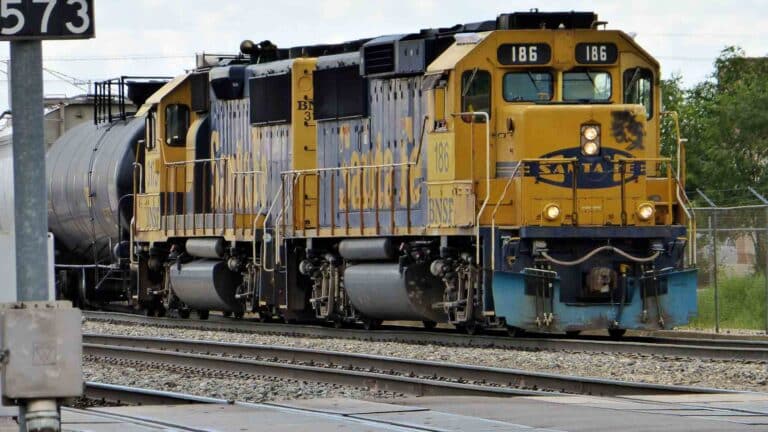 Um trem de carga amarelo e azul com o número 186 na frente, movendo-se ao longo dos trilhos, simboliza dois fatores essenciais na importação logística.