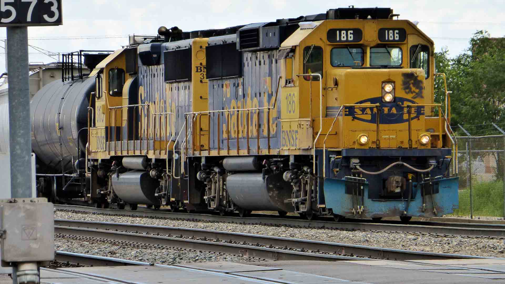 Um trem de carga amarelo e azul com o número 186 na frente, movendo-se ao longo dos trilhos, simboliza dois fatores essenciais na importação logística.
