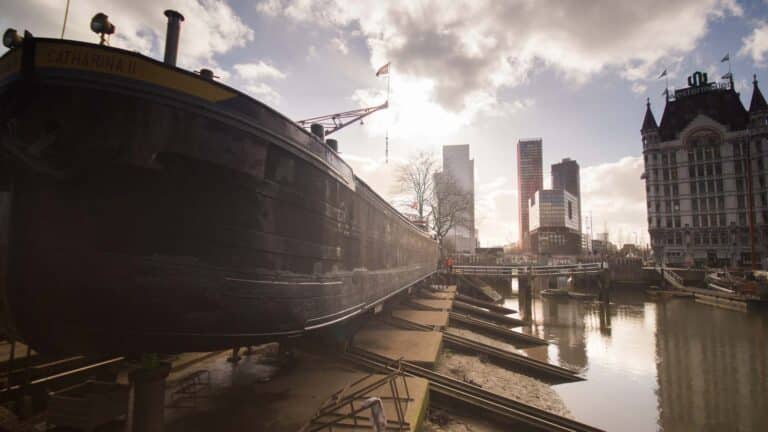 O barco chamado “Catharina II” repousa no cais perto da água em uma área urbana, com edifícios modernos erguendo-se sob um céu nublado, simbolizando as vastas oportunidades de importação no horizonte à medida que nos aproximamos de 2025.