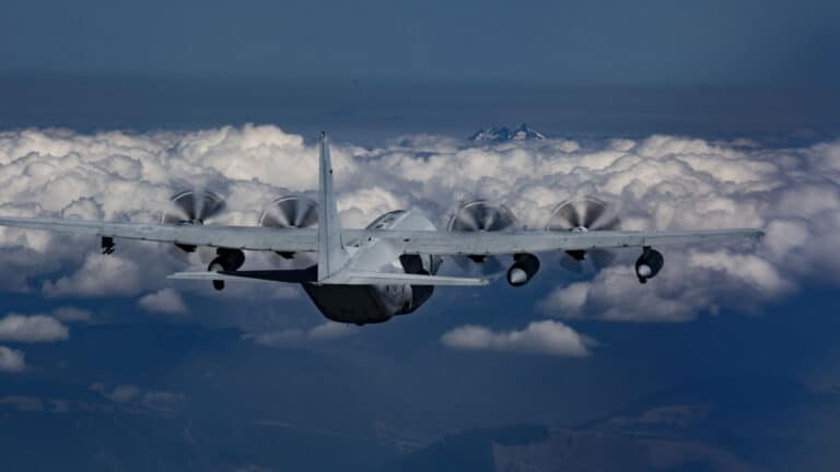 Uma aeronave militar com quatro hélices voa acima de uma densa camada de nuvens, empregando estratégias para navegar pelos céus, com um pico de montanha distante visível ao fundo.