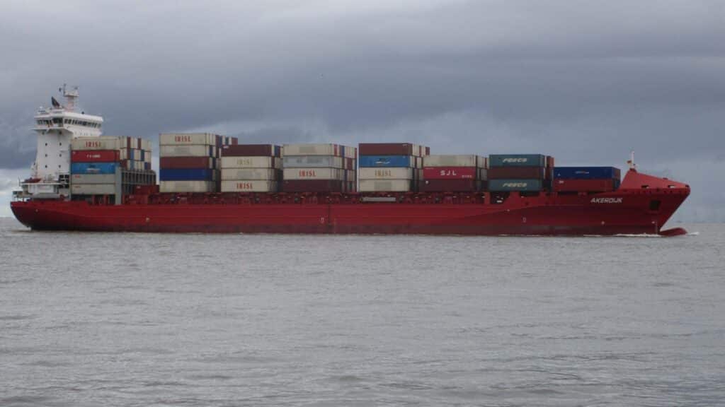 Navio de carga no mar sob um céu nublado, carregado com contêineres empilhados, navegando estrategicamente para reduzir os custos de frete até 2025.