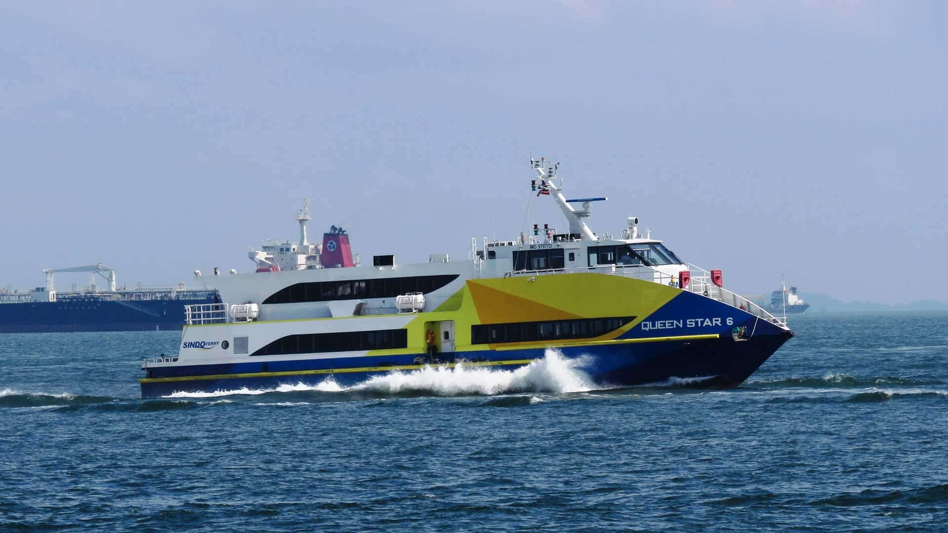 Uma balsa amarela e azul chamada "Queen Star 2" desliza pela água, simbolizando o sucesso em viagens marítimas, com navios de carga visíveis ao fundo sob um céu parcialmente nublado.