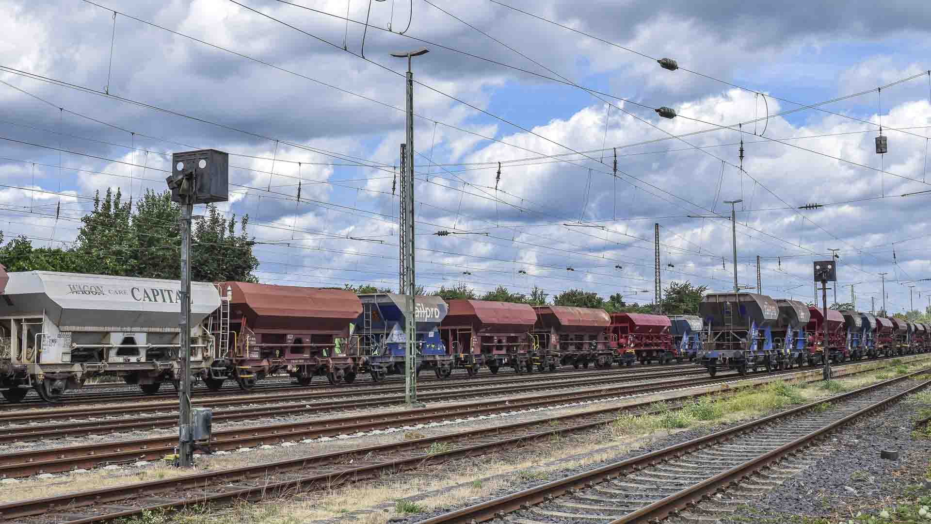 Um trem de carga, vital para grandes empresas, transporta vagões de carga coloridos ao longo dos trilhos ferroviários sob um céu nublado, simbolizando o processo dinâmico de importação de mercadorias através de fronteiras.