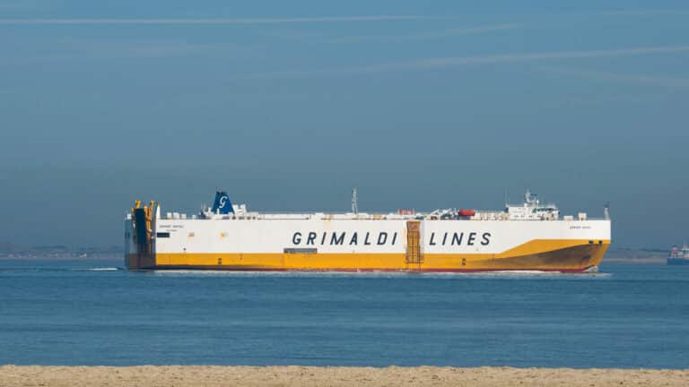 O grande navio de carga com "Linhas Grimaldi" estampado na lateral navega suavemente em águas calmas sob o céu claro de 2024, uma presença serena que lembra navios que se dirigem a eventos de prestígio como a Feira de Cantão.