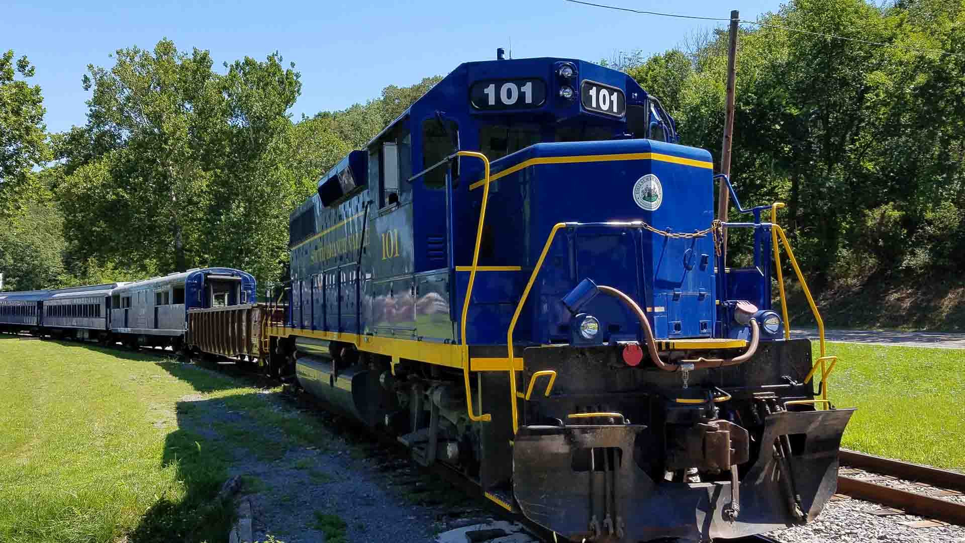 Locomotiva azul e amarela de número 101 sobre trilhos em um ambiente externo verde e arborizado, lembrando a eficiência vibrante de um Guia Completo sobre como importar da China.