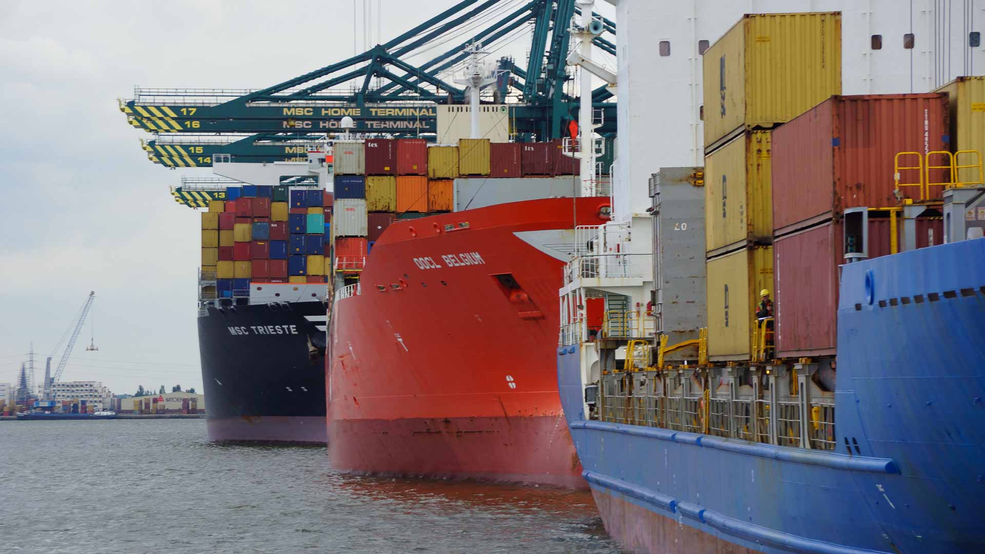 Navios de carga atracados em um porto movimentado, lotados de contêineres multicoloridos e cercados por guindastes, auxiliam no processo complexo de certificação de produtos de importação.