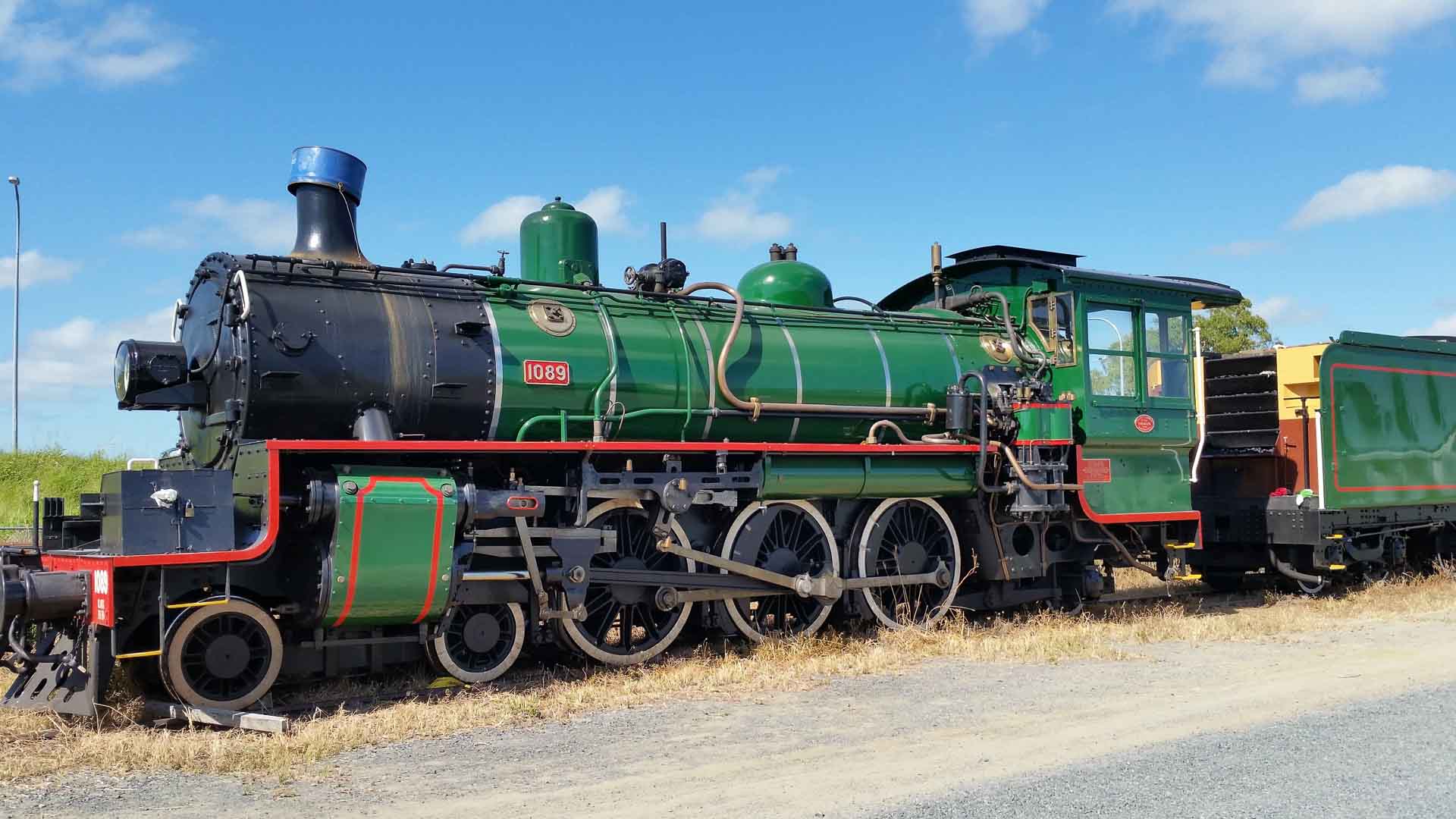 Uma locomotiva a vapor verde com detalhes em vermelho e preto está estacionada em um caminho de cascalho sob um céu azul, oferecendo uma viagem atemporal que lembra a rica história da importação.