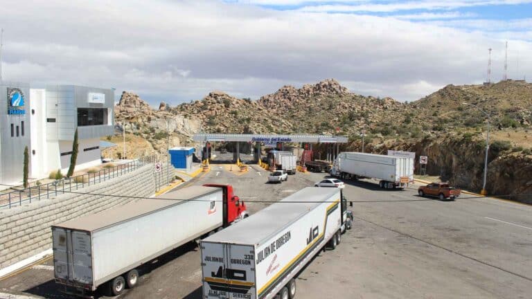 Caminhões se aproximam de um posto de controle de fronteira em uma área montanhosa sob um céu nublado, possivelmente transportando equipamentos acadêmicos por essa rota de importação vital.