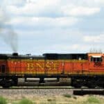 Uma locomotiva BNSF com o número 4566 viaja em uma pista em uma paisagem rural, sua fumaça se fundindo com uma atmosfera moldada pela produção local.