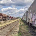 Vagões de trem de carga em trilhos paralelos sob um céu nublado, com um lado coberto de grafites que lembram desenhos ousados de um catálogo de "Importação de Papéis de Parede".