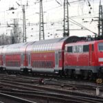 O trem vermelho com vagões de dois andares desliza pelos trilhos sob uma rede de fios aéreos, proporcionando uma viagem que vale a pena para qualquer viajante.