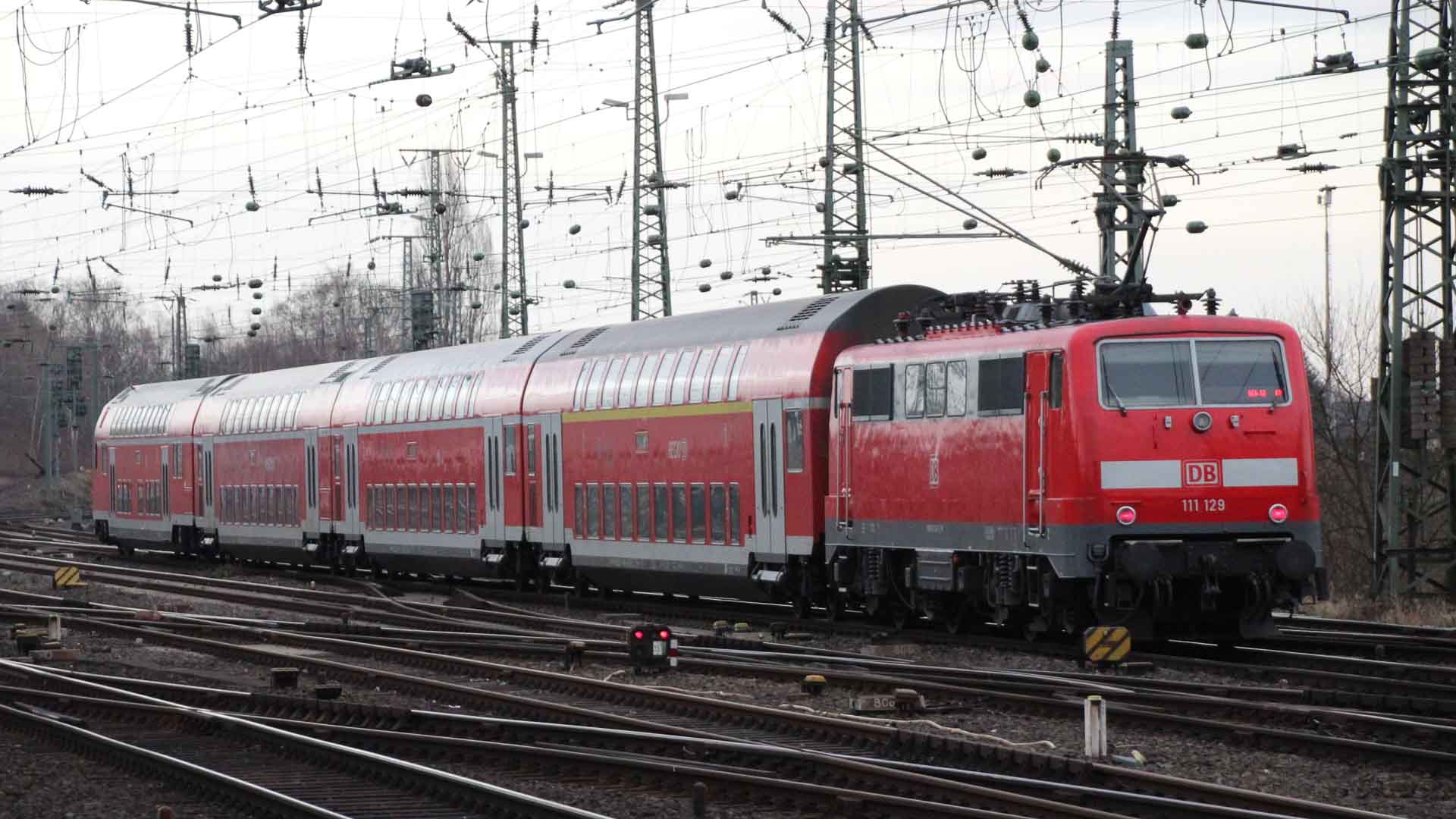 O trem vermelho com vagões de dois andares desliza pelos trilhos sob uma rede de fios aéreos, proporcionando uma viagem que vale a pena para qualquer viajante.