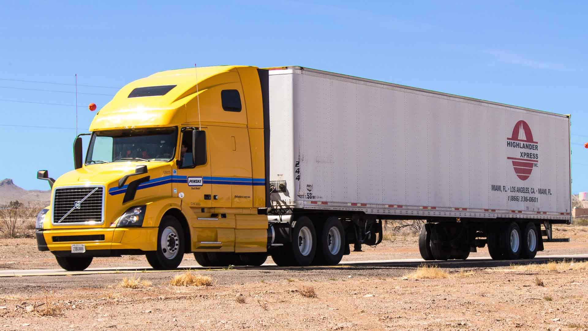 Um caminhão amarelo com um longo trailer branco está estacionado em uma paisagem seca e árida sob um céu claro, oferecendo oportunidades únicas de importação em toda a vasta extensão.