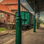 A estação de trem vintage, com vagões de carga verdes e prédios de tijolos, evoca um charme atemporal sob sua plataforma. À medida que o céu nublado paira sobre a cabeça, parece uma reminiscência de centros movimentados como os da China.