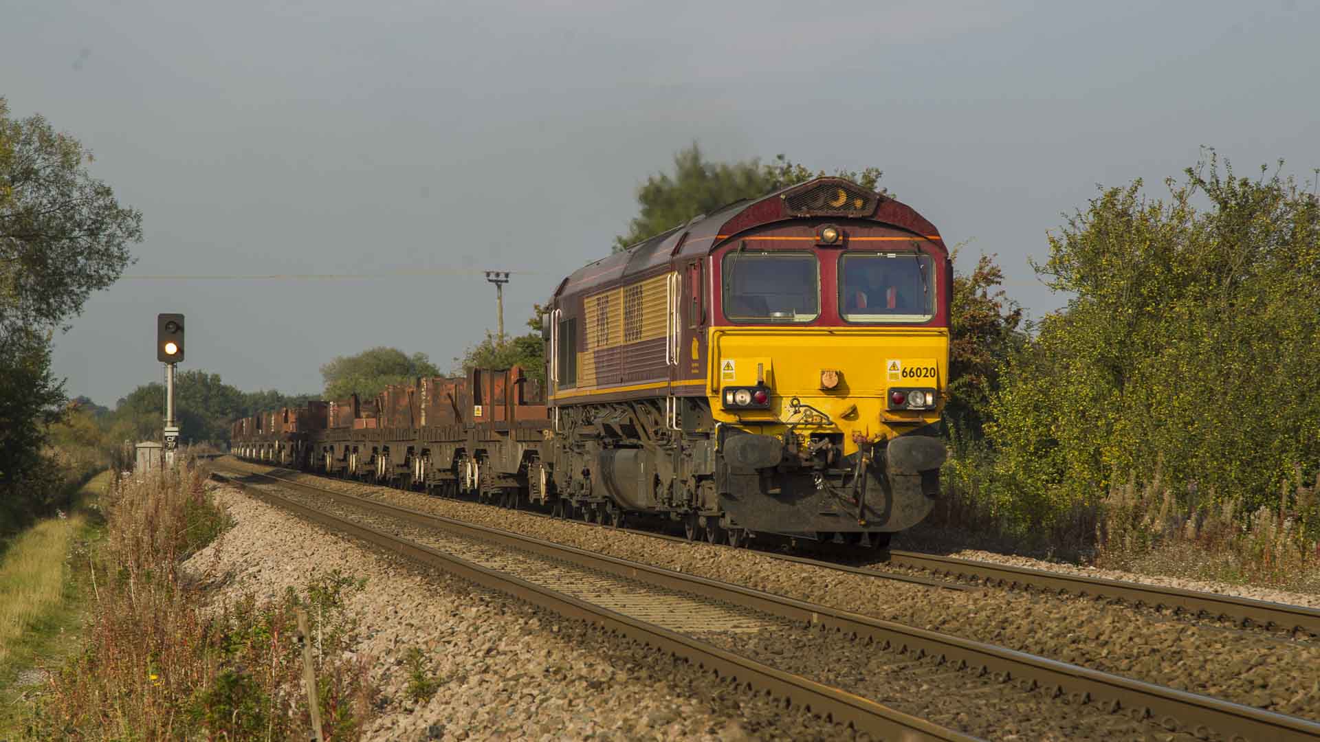 Em 2025, um trem de carga com uma carga aberta de metal viaja em uma ferrovia através de uma paisagem rural sob um céu limpo, mostrando a melhor forma de negociar com fornecedores transportando mercadorias de forma eficiente.