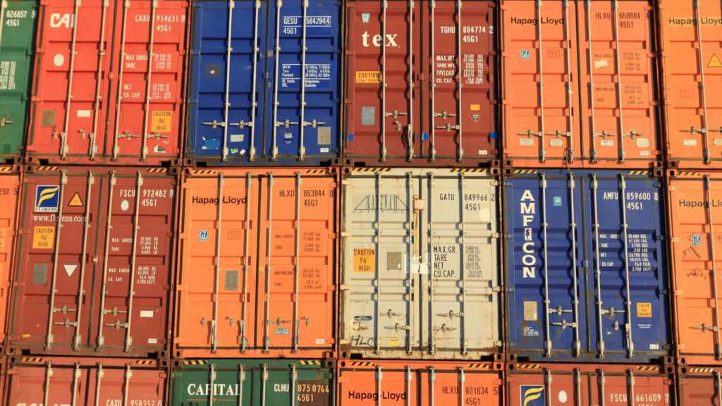 Contêineres de transporte coloridos empilhados com vários logotipos de empresas e números de identificação estão prontos para exportação, exibindo a melhor forma de organização. Perfeito para aqueles que buscam pesquisar na China de forma eficiente.