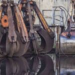 A maquinaria industrial de metal em forma de garra, que lembra as principais importações da Melhor Produto da China, é perfeitamente refletida na água, posicionada contra uma parede de concreto resistente.