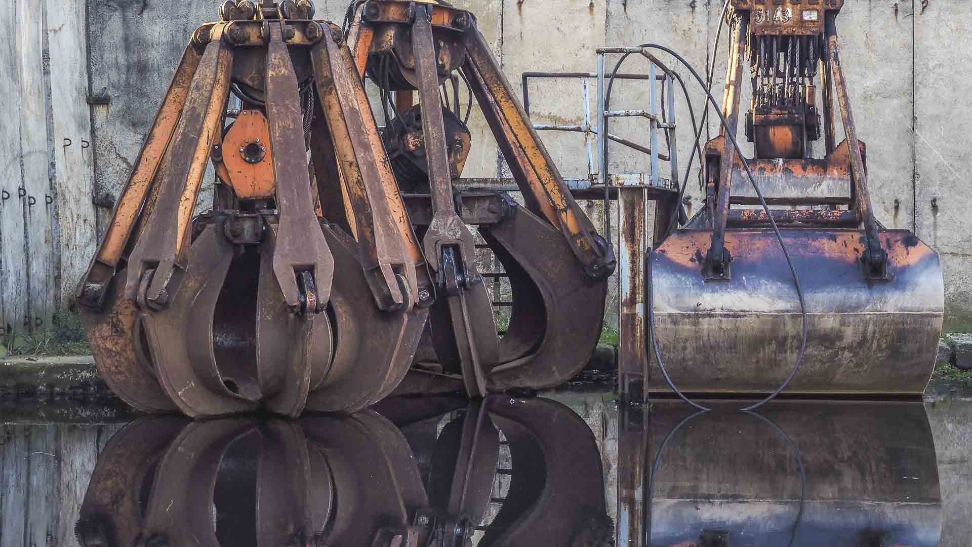 A maquinaria industrial de metal em forma de garra, que lembra as principais importações da Melhor Produto da China, é perfeitamente refletida na água, posicionada contra uma parede de concreto resistente.