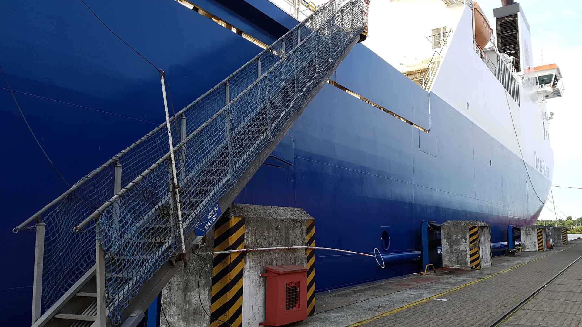 Um navio azul e branco está atracado no porto, com sua passarela de metal se estendendo para a lateral, pronto para receber mercadorias que serão importadas da China em 2024.