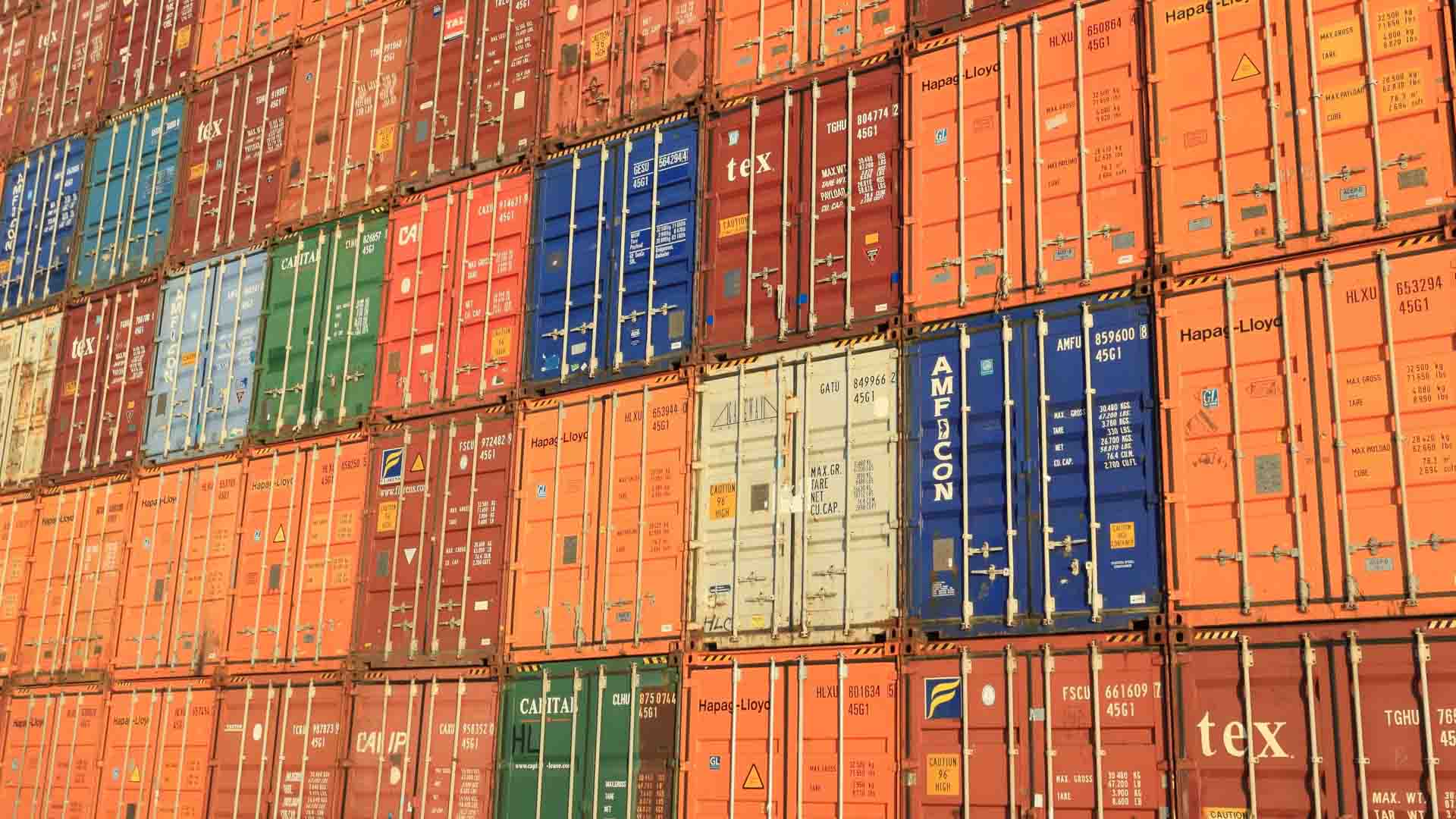 Contêineres de transporte empilhados em várias cores e tamanhos, dispostos em um padrão de grade, simbolizam as infinitas oportunidades que a importação trará até 2025.
