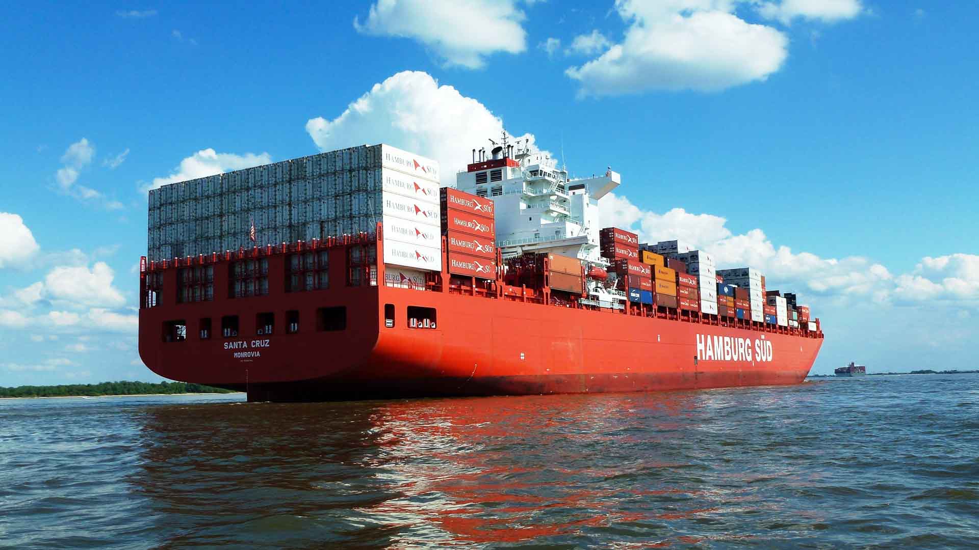 Um grande navio porta-contêineres vermelho, envolvido no processo de importação, transporta inúmeros contêineres de carga em águas calmas sob um céu parcialmente nublado, garantindo que todos os Órgãos Anuentes necessários sejam atendidos.