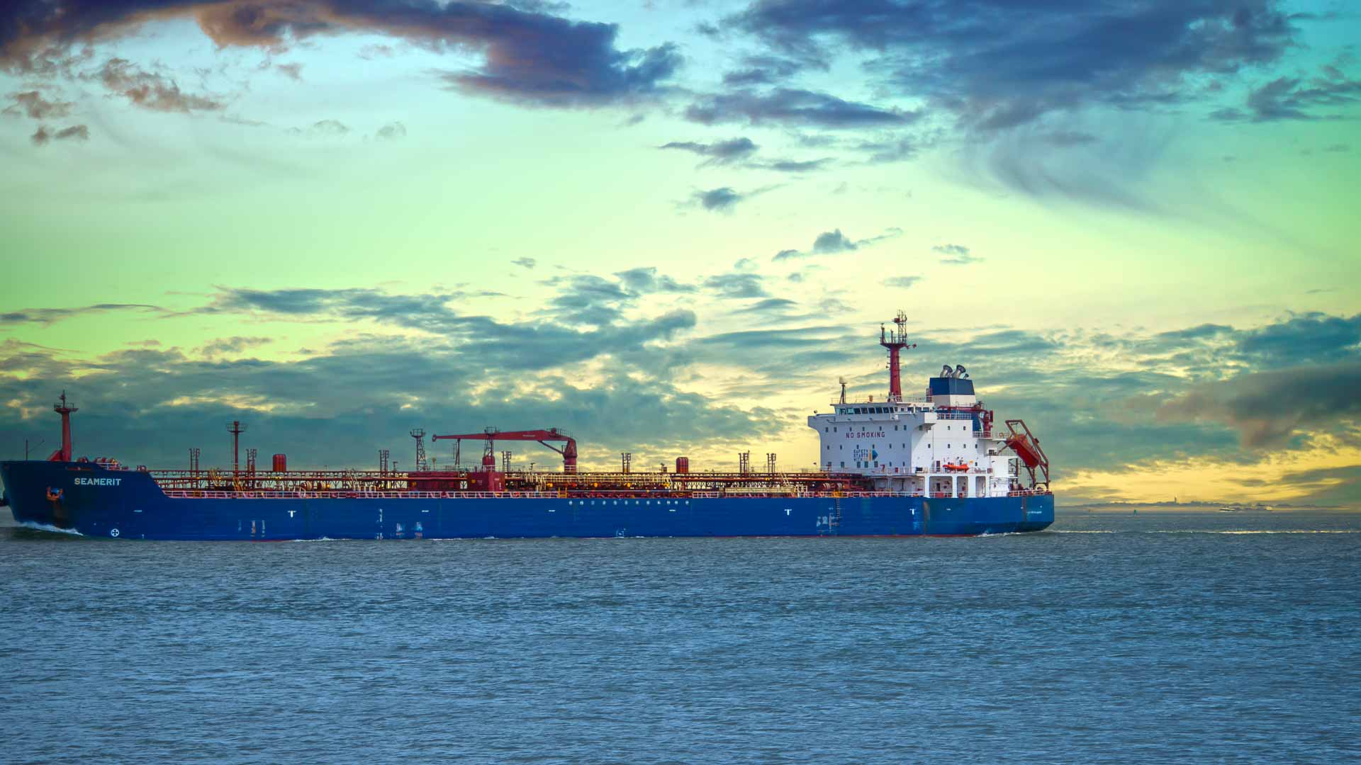 Enquanto o sol se põe sob um céu nublado, um grande navio de carga azul, transportando produtos de alta demanda para 2025, navega em um mar calmo.