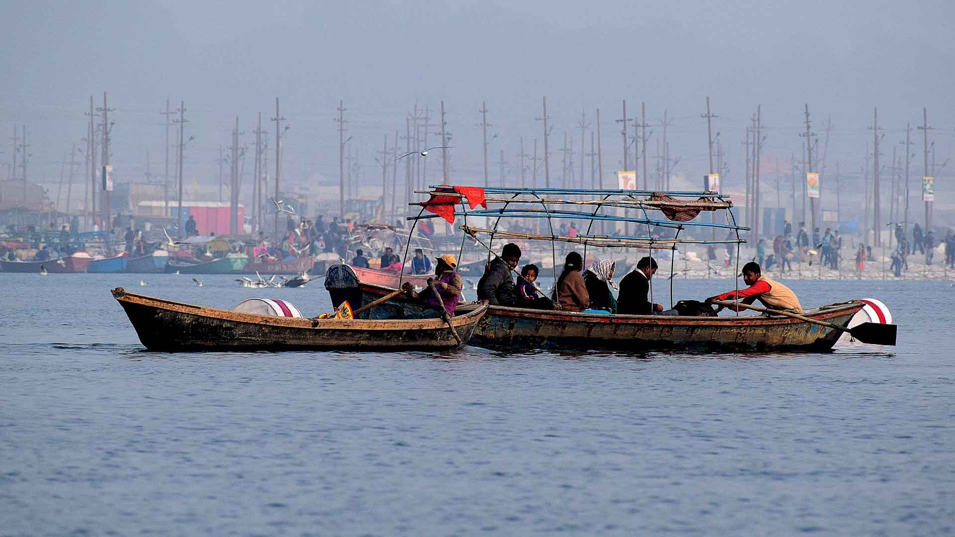 Um grupo de pessoas em um barco de madeira navega pelo rio, personificando a dedicação semelhante à Regra das 10 Mil Horas. Mais alguns barcos flutuam por perto, importando uma sensação de tranquilidade contra a costa distante suavemente delineada ao fundo.
