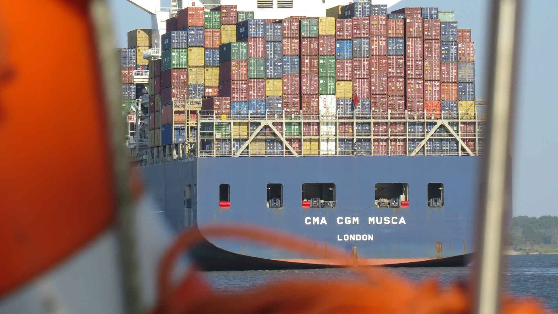 Vista de um grande navio de carga, o CMA CGM Musca, carregado com contêineres empilhados, capturada de um barco próximo a caminho da Feira de Cantão 2025. Perfeito para aqueles que buscam motivos para visitar e testemunhar o comércio global em ação.