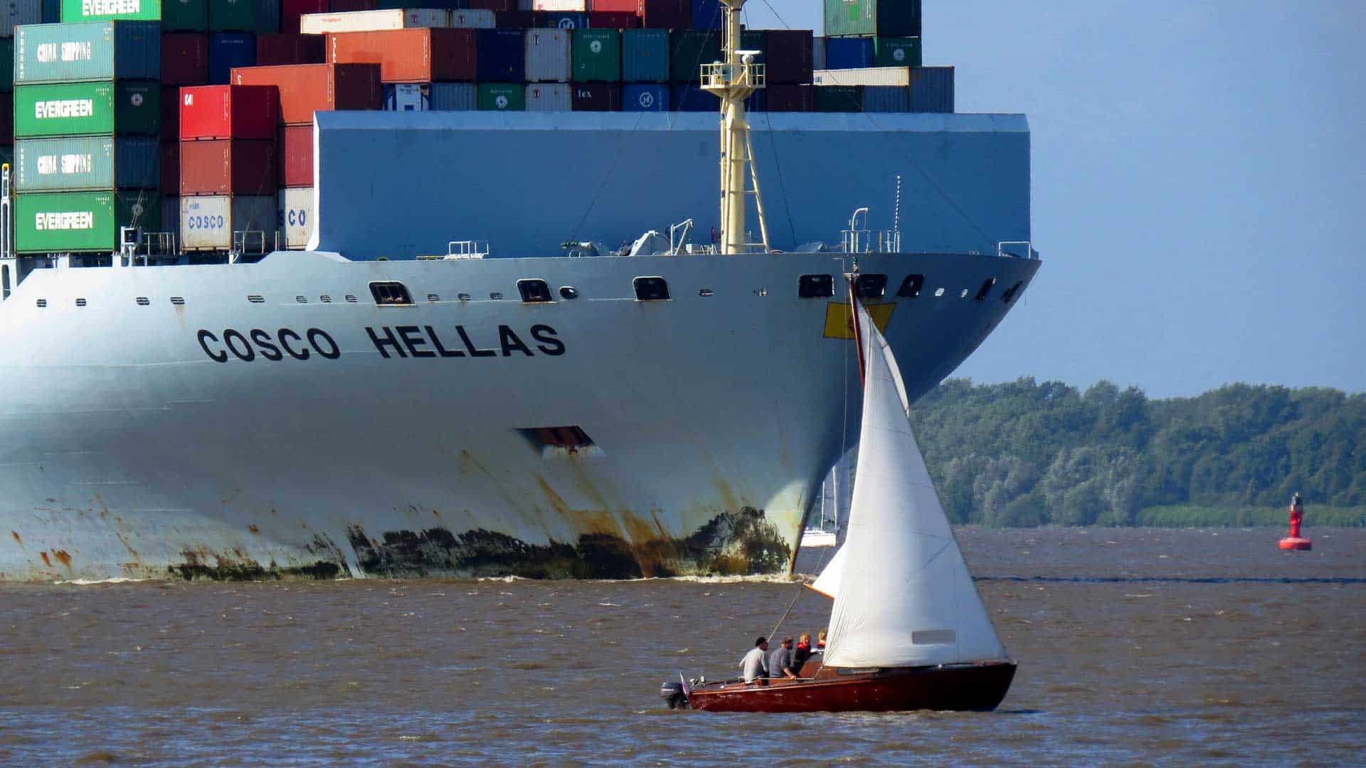 Um grande navio porta-contêineres com o rótulo "COSCO HELLAS" passa perto de um pequeno veleiro na água, uma cena que pode lembrar o poder do Evernote de aumentar a produtividade ao navegar por tarefas grandes e pequenas.