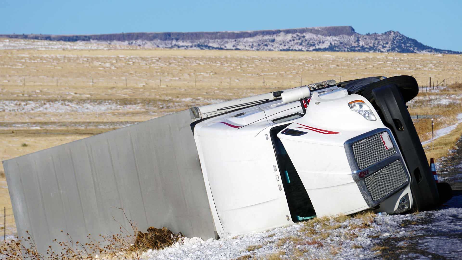 Um caminhão branco tombado em uma estrada coberta de neve em 2025, com um campo aberto e uma mesa ao fundo, enquanto a Grandes Importadores se esforça para competir em condições desafiadoras.