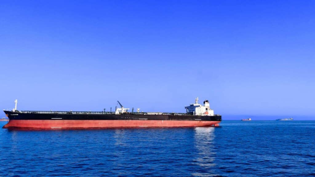 Um grande navio de carga com casco vermelho e estrutura superior preta, essencial para reuniões eficientes em rotas de importação marítima, navega em um mar azul calmo sob um céu limpo.