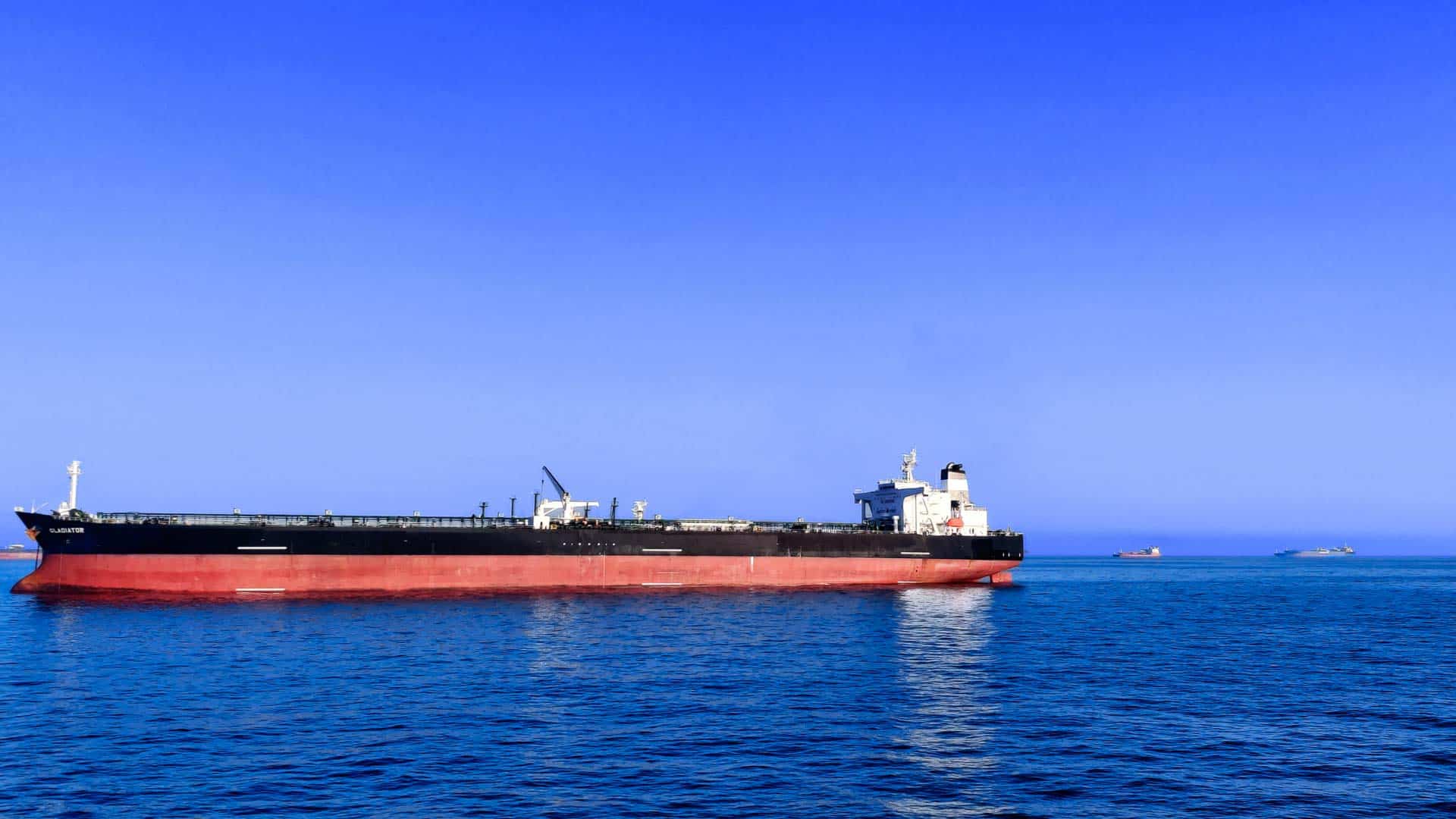 Um grande navio de carga com casco vermelho e estrutura superior preta, essencial para reuniões eficientes em rotas de importação marítima, navega em um mar azul calmo sob um céu limpo.