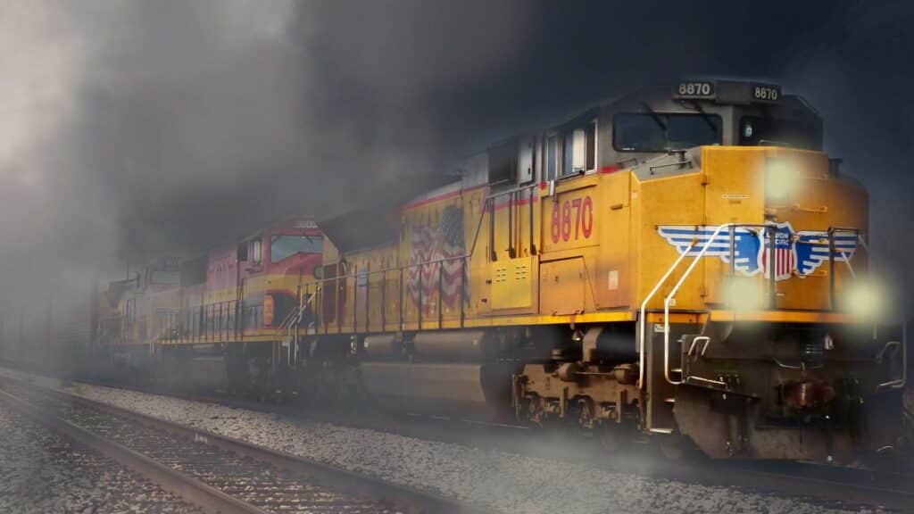 Um trem de carga amarelo viaja sobre trilhos em meio à fumaça densa, com um logotipo e número 8670 visíveis na locomotiva da frente, uma reminiscência de produtos que você frequentemente encontra ao optar por importar e vender produtos.