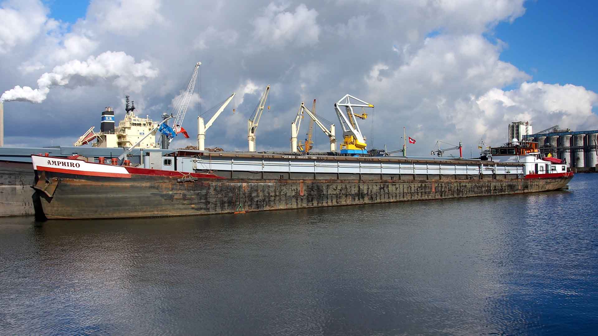 O grande navio de carga, Saporro, atracou no porto, pronto para sua jornada em 2024. Guindastes e edifícios industriais apareciam ao fundo sob um céu parcialmente nublado, destacando a cena movimentada de importação de mercadorias da China.