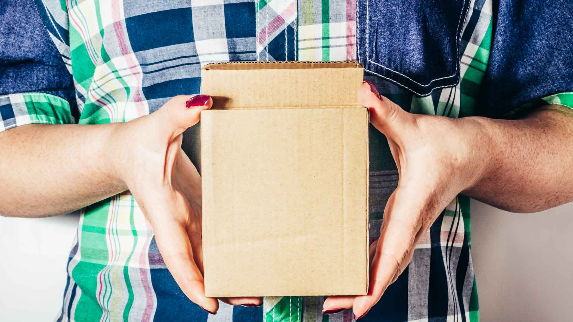 Uma pessoa vestindo uma camisa xadrez segura uma pequena caixa de papelão, talvez cheia de produtos importados que prometem alta margem de lucro.