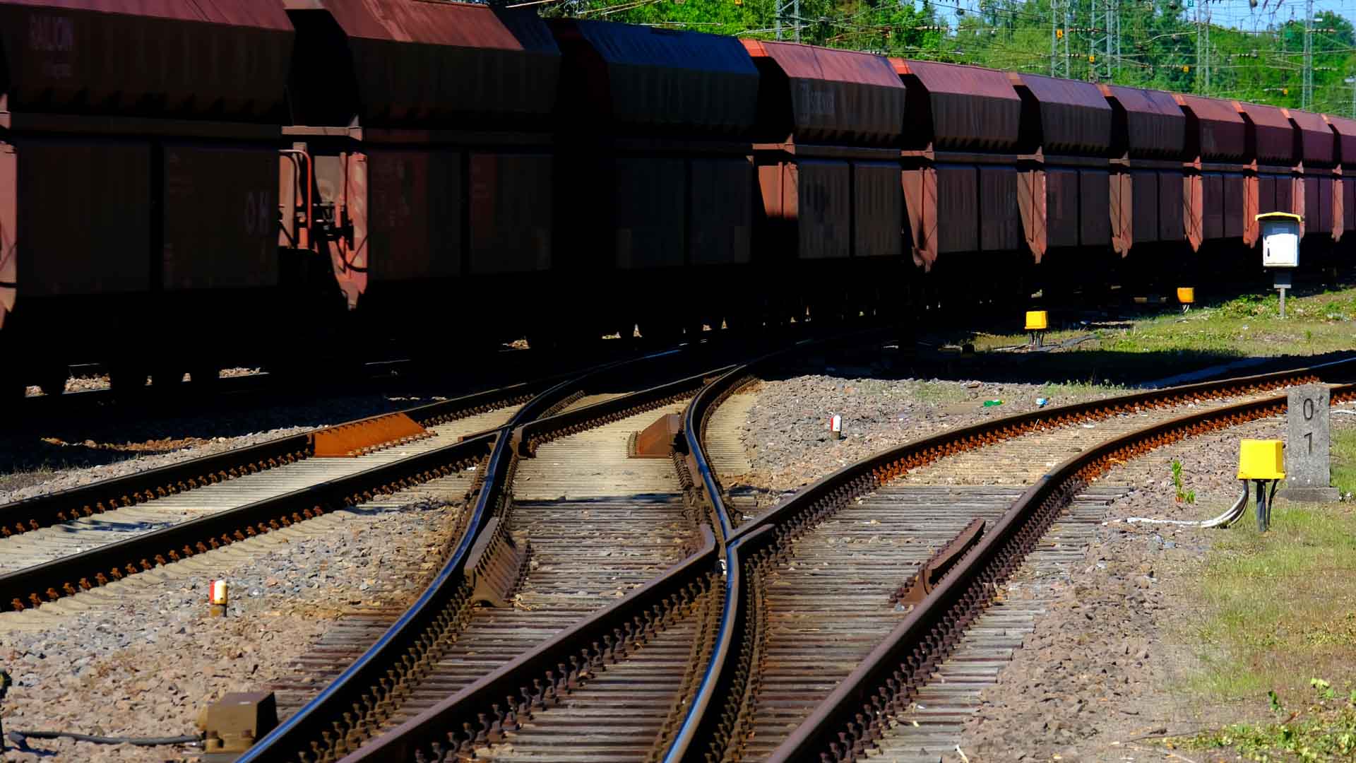 Um trem de carga sobre trilhos ferroviários em um ambiente ensolarado ao ar livre, com vegetação ao fundo, simboliza a importância dos produtos tecnológicos de ponta que devem revolucionar as indústrias até 2025.