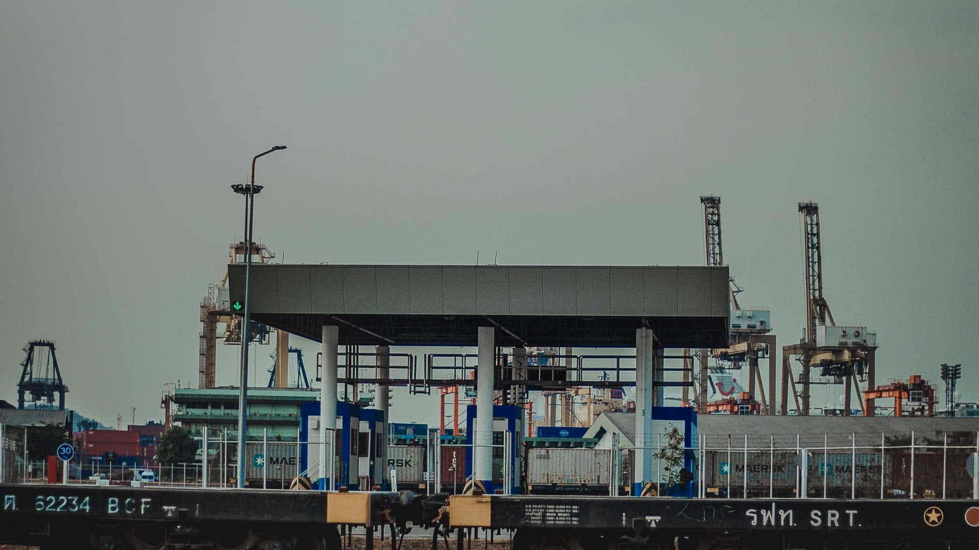 Cena de porto industrial com guindastes e contêineres de transporte, onde cada passo do processo é crucial. O primeiro plano apresenta equipamentos e estruturas. O céu nublado adiciona um tom suave, muito parecido com seguir um passo a passo ao navegar por complexidades como importar secadores de cabelo.