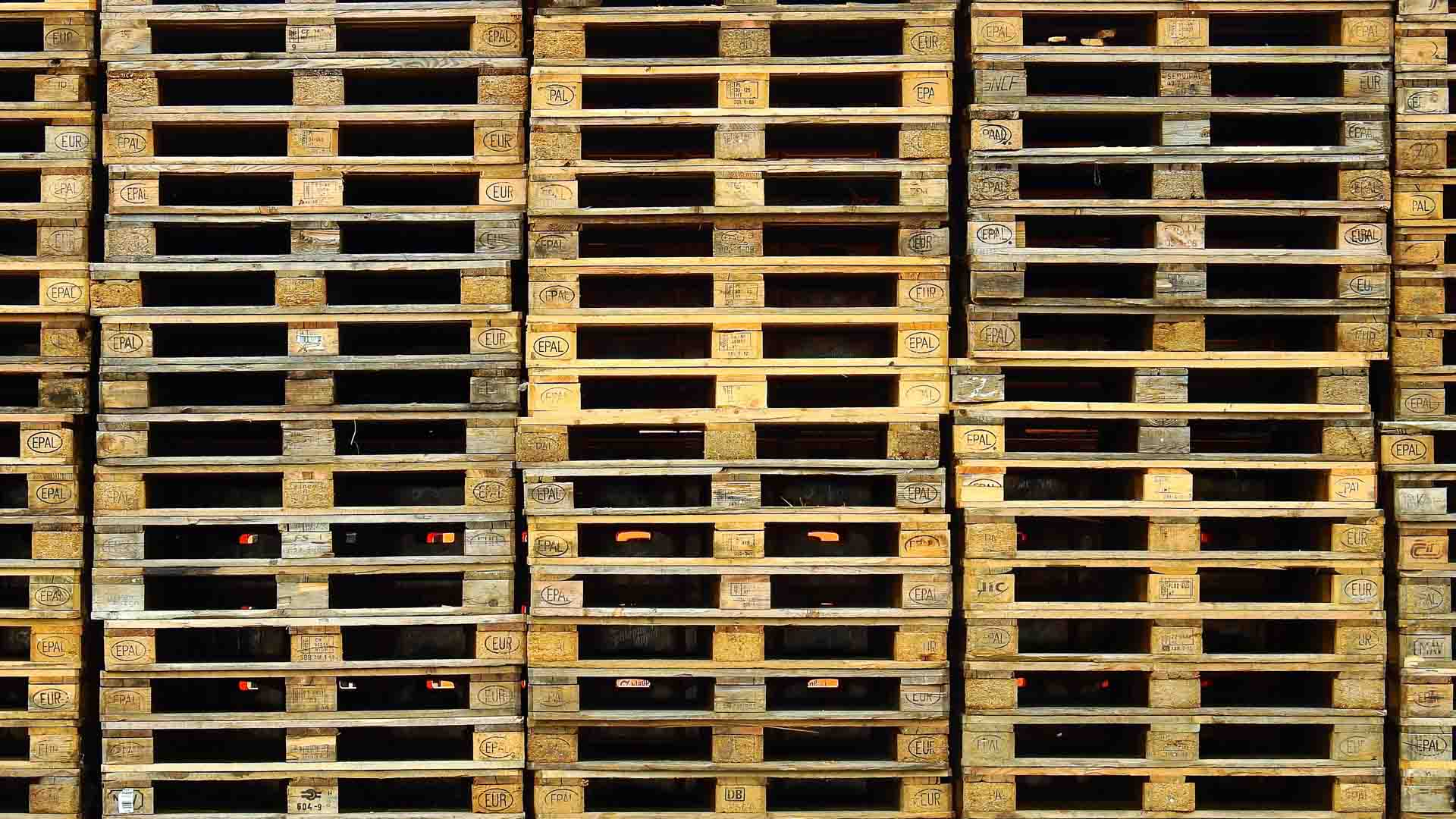 Paletes de madeira empilhados e dispostos em fileiras, apresentando um padrão e textura repetitivos, são essenciais para selecionar produtos com precisão e eficiência.