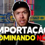 Imagem de um homem com boné preto explicando sobre importação, com um fundo aéreo de um porto cheio de contêineres e um guindaste azul e amarelo. O texto na imagem diz "IMPORTAÇÃO. DOMINANDO NCM", indicando um guia sobre a classificação de mercadorias na importação.